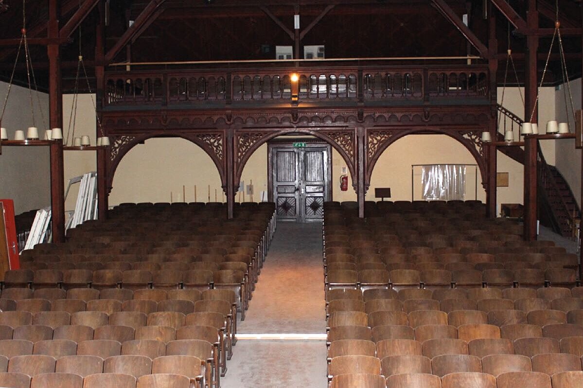 Die große, baufällige Aula aus dunklem Holz. 