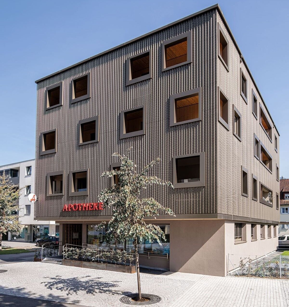 Mehrstöckige Apotheke mit moderner Fassade und Baum.