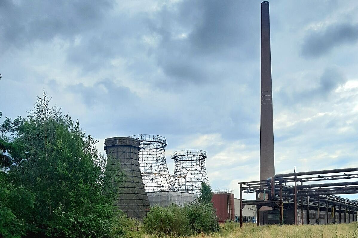 Stillgelegte Industrieanlage mit Kühltürmen und hohem Schornstein unter bewölktem Himmel.