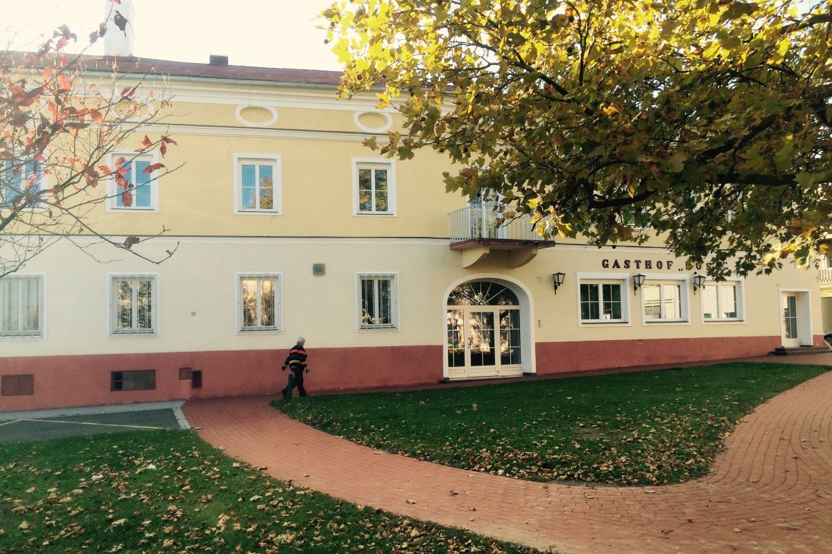 Wohnhaus Rose vor dem Umbau. 1 stöckiges Haus, gelb-beige Fassade, kleiner Balkon und eine Rasenfläche davor.