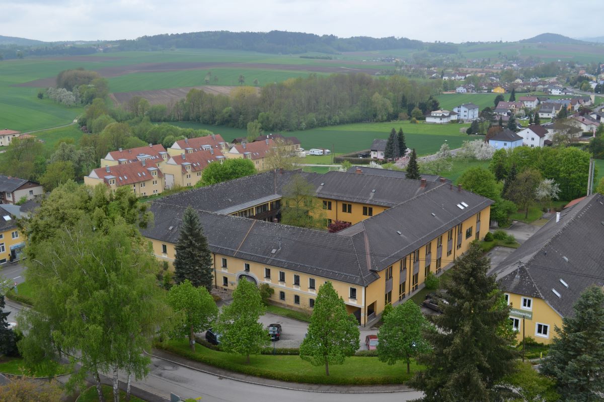Das einstöckiges gelbes Gemeindezentrum im Hof in Katsdorf von aussen, umgeben von Bäumen.
