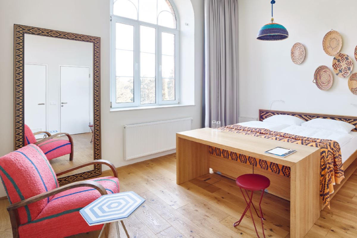 Die Hotelzimmer nach der Revitalisierung Das Hotelzimmer nach der Revitalisierung: hell, großer Spiegel davor ein bequemer Sessel, Doppelbett und Applikationen an der Wand.