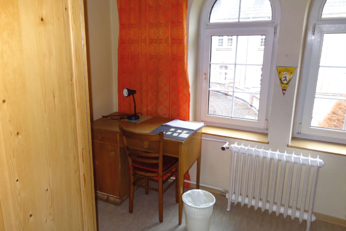 Hotelzimmer vor dem Umbau. Kleiner Holzschreibtisch im Eck neben dem Fenster, aber hinter dem großen Holzkasten.